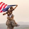 Man in army uniform with boy on his shoulders holding American flag